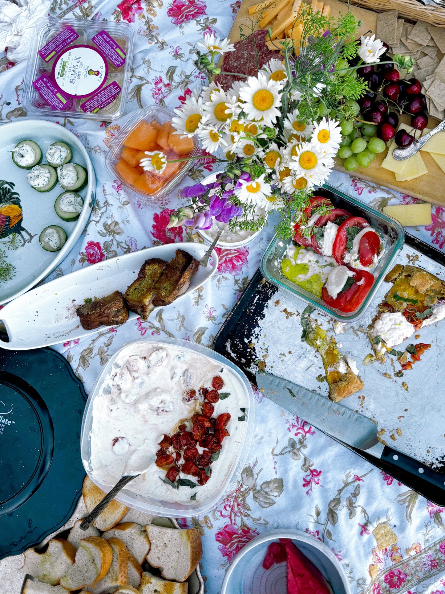 Outdoor picnic setup with food and cutlery on a floral blanket