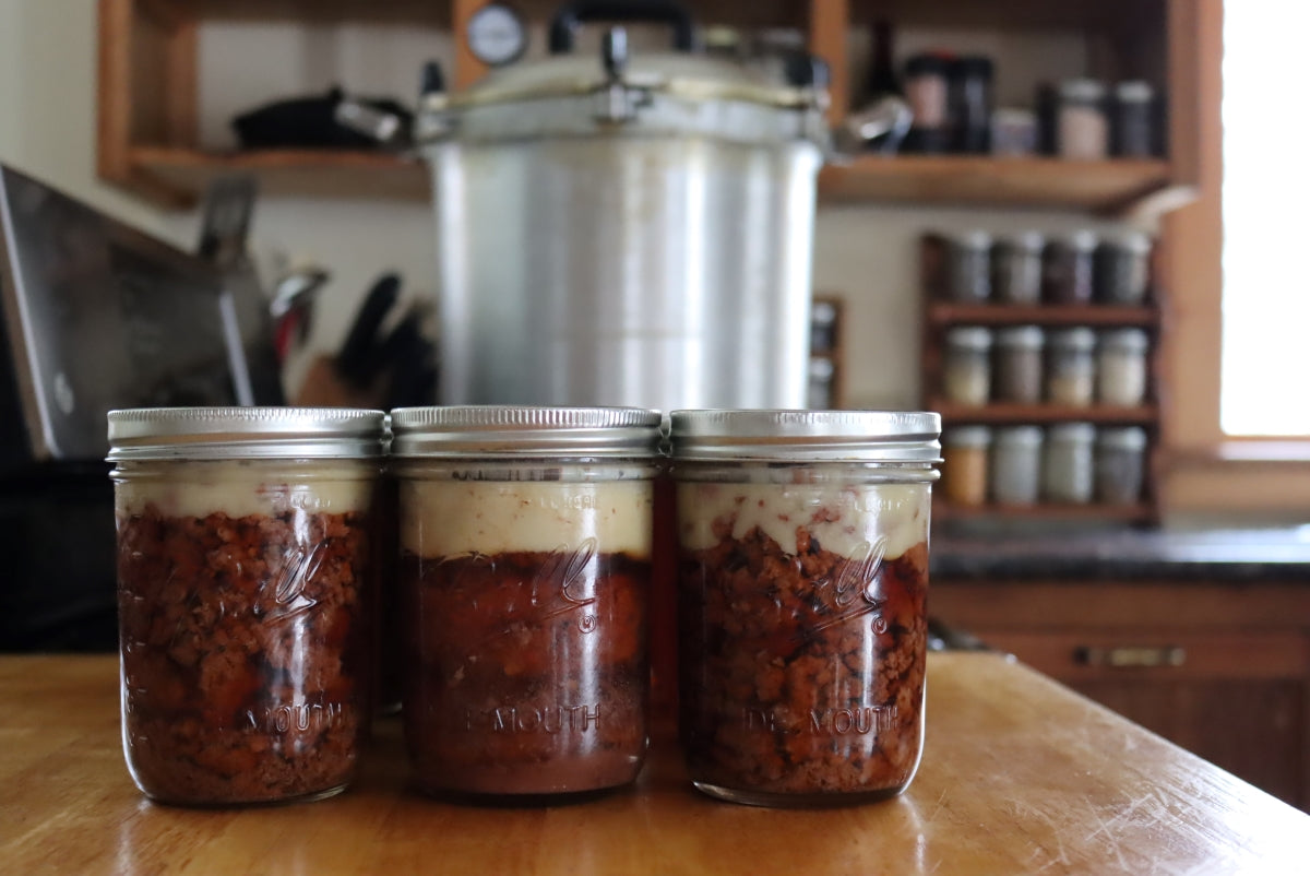 Three jars of food on a kitchen counter with a pressure cooker in the background.