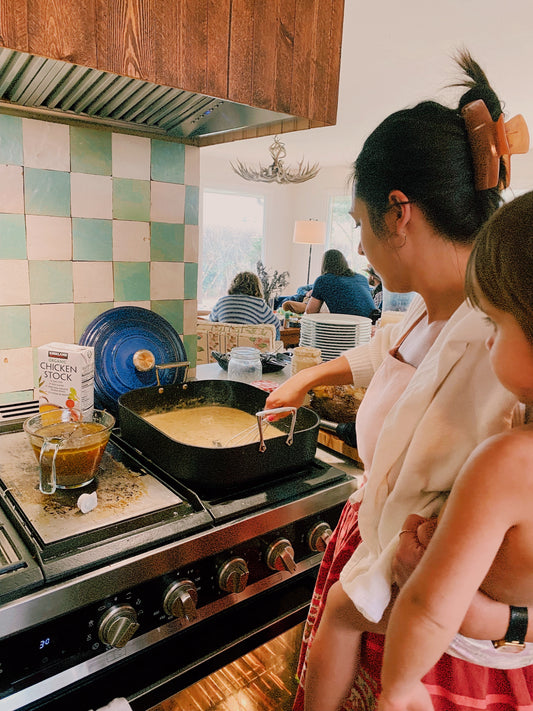 Woman cooking in a kitchen with a child by her side.