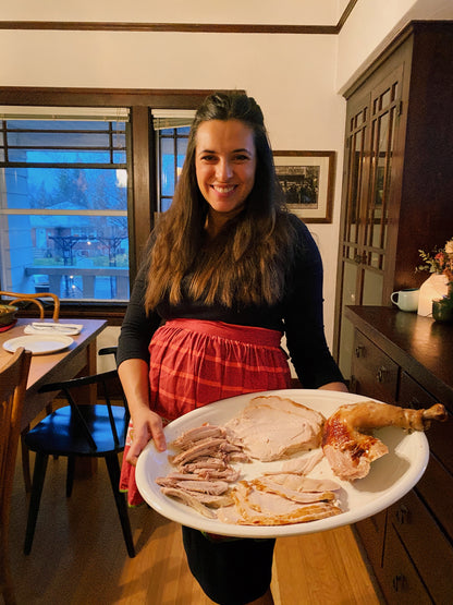 Woman holding a platter of sliced turkey in a kitchen.